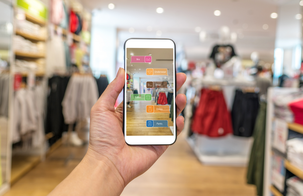 image of a hand holding a phone up in front of them while they're in a clothing store, and the phone is showing them different augmented reality options, something brands should keep in mind for their influencer marketing strategy

